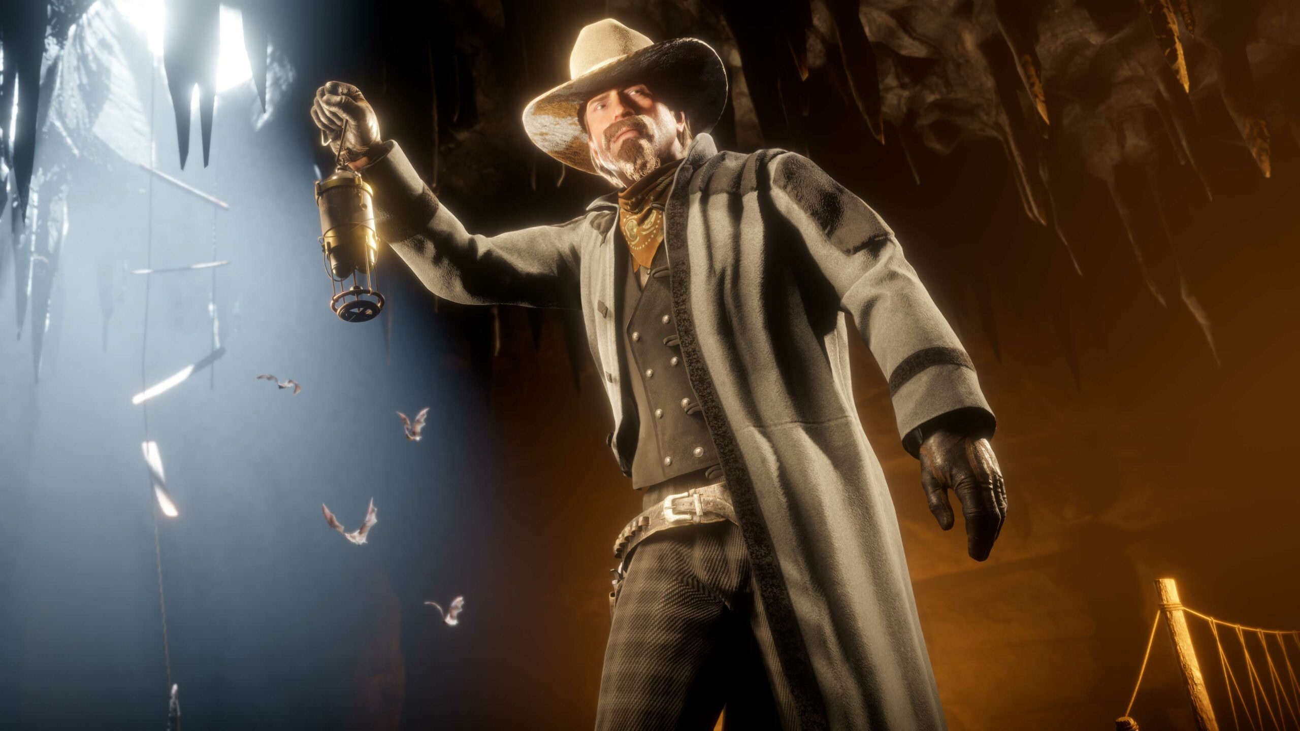 Personagem de Red Dead Online segura uma lanterna dentro de uma caverna iluminada por chamas, enquanto morcegos voam em direção à claridade do lado de fora.